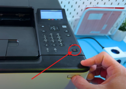 En h&aring;nd trykker p&aring; str&oslash;mknappen p&aring; Canon-skriveren.